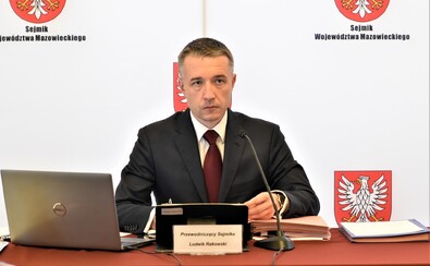 Przewodniczący sejmiku Ludwik Rakowski siedzi za stołem. Przed nim stoi otwarty laptop, a za nim - banery z godłem mazowsza