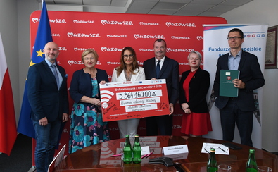 Wicemarszałek Raboszuk i członek zarządu Elżbieta Lanc pozują do zdjęcia z czekiem z czterema przedstawicielami beneficjenta.