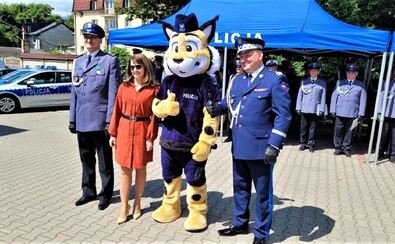 Janina Ewa Orzełowska stoi obok dwóch funkcjonariuszy w galowych mundurach. Między nimi jest trzeci mężczyzna w przebraniu maskotki policji - pluszowego tygrysa w policyjnym mundurze.