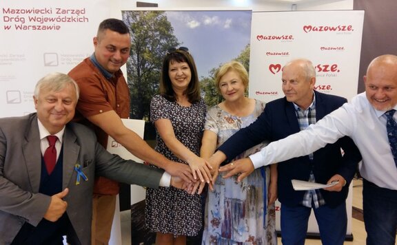 Janina Ewa Orzełowska i Elżbieta Lanc składają prawe ręce - razem z 4 beneficjentami - w geście jedności. Wszyscy się uśmiechają