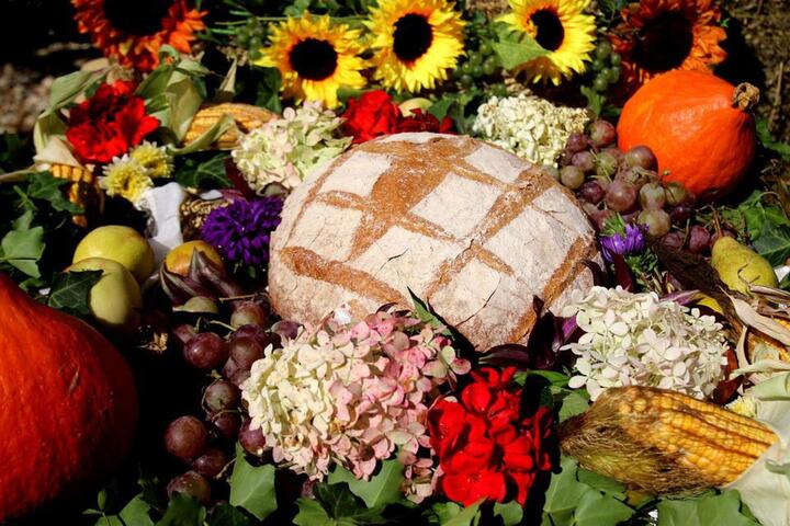 Wielki bochen chleba otoczony kwiatami, owocami i warzywami