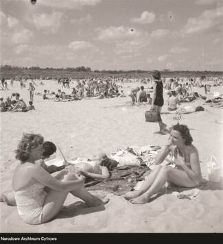 Kobiety w kostiumach kąpielowych siedzą na kocu na nadmorskiej plaży