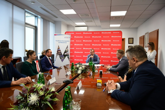 Na zdjęciu spotkanie przy stole, na środku wicemarszałek Wiesław Raboszuk, po jego prawej i lewej stronie sześciu beneficjentów. W tle trzy kobiety.