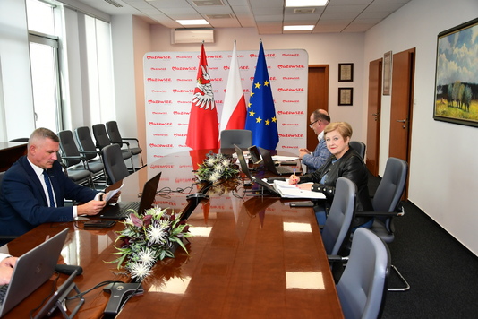 Widok na trzy osoby z Zarządu Województwa Mazowieckiego: Ludwik Rakowski, Elżbieta Lanc, Wiesław Raboszuk siedzących przy stole z laptopami podczas zdalnego posiedzenia Sejmiku Mazowsza.