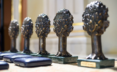 cztery statuetki nagrody Norwida ustawione obok siebie w rzędzie. Przed nimi w zamkniętym etui leżą medale.