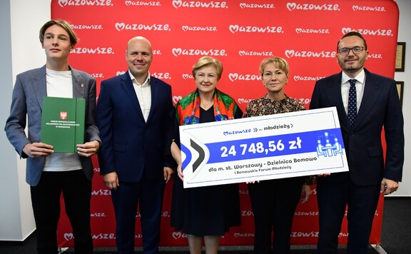 Elżbieta Lanc pozuje z czterema przedstawicielami beneficjenta. Trzyma razem z jedną z nich czek symboliczny na ponad 24 tys. zł
