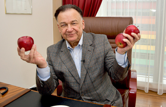 Mężczyzna siedzi przy biurku i trzyma trzy jabłka