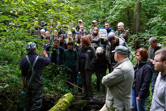 Grupa ludzi w lesie przygląda się mężczyźnie