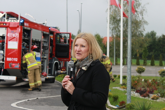 Kobieta udziela wywiadu. W tle widać strażaków przy samochodzie pożarowym