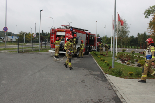 Wóz strażacki, przy którym widać strażaków w ubraniu bojowym