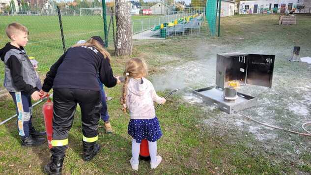 Strażak pokazuje małej dziewczynce gaszenie ognia w zajętym piecu