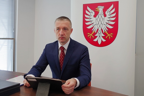 Przewodniczący sejmiku Ludwik Rakowski siedzi przy biurku przed tabletem. W tle widać herb Mazowsza.