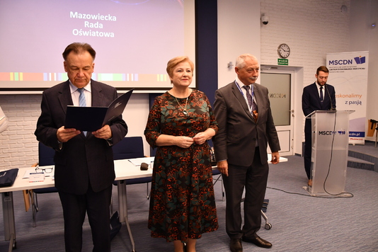 Marszałek trzyma przed sobą otwartą teczkę z listem. Obok niego stoi Elżbieta Lanc i Krzysztof Skolimowski
