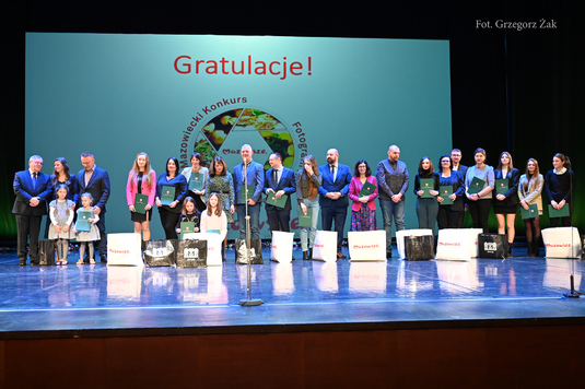 Na zdjęciu grupa osób z nagrodami pozują do zdjęcia na scenie