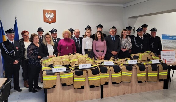 Orzełowska pozuje do zdjęcia ze strażakami z gminy Sarnaki. Przed nimi na stole rozłożony jest nowy sprzęt