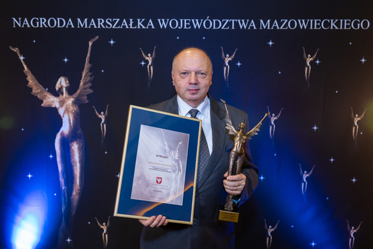 Przy mikrofonie stoi laureat Zbigniew Kołaczek. W rękach trzyma dyplom i statuetkę