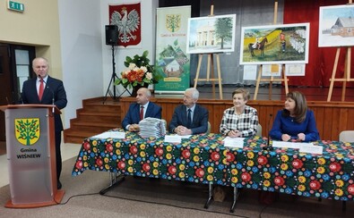 Lanc i Orzełowska siedzą przy stole konferencyjnym wraz z trzema przedstawicielami beneficjentów. Przy mównicy obok stoi mężczyzna