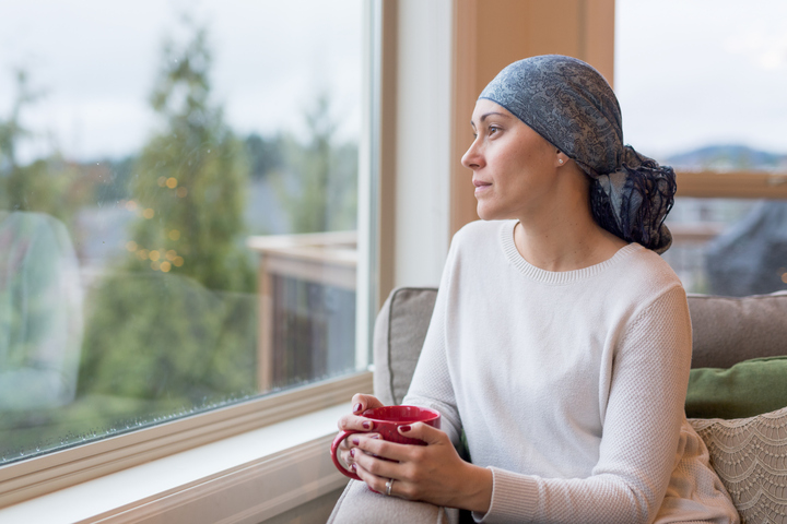 Kobieta z rakiem pije filiżankę herbaty i wygląda przez okno.