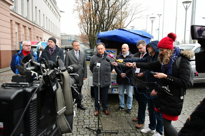 Grupa mężczyzn podczas deszczowej pogody odpowiada na pytania dziennikarzy.