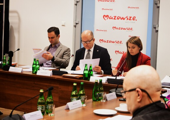 Dyrektor Marcin Wajda siedzi obok wojewody mazowieckiego. Obaj przeglądają dokumenty.