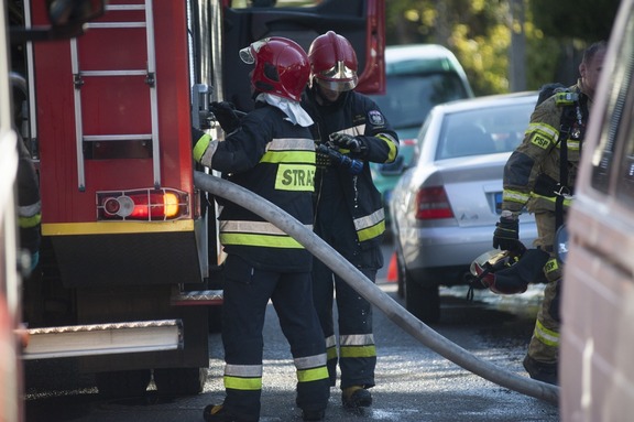 Dwaj strażacy wyjmują węża pożarniczego z wozu strażackiego