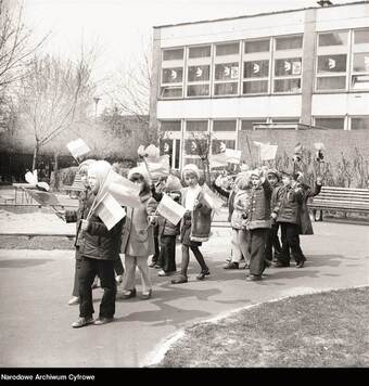przedszkolaki w biało-czerwonymi chorągiewkami stoją przed budynkiem przedszkola