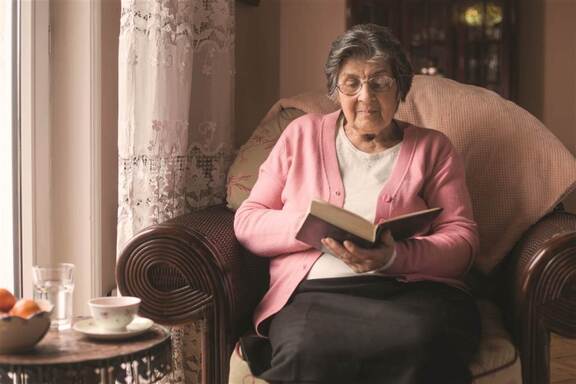 starsza kobieta siedzi na fotelu i czyta książkę