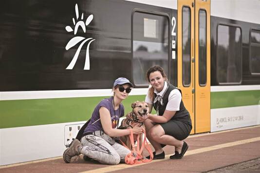 Dwie kobiety na peronie pozują do zdjęcia z psem.