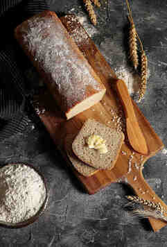 Bochenek chleba z odkrojonymi dwiema kromkami, na których leży kawałek masła