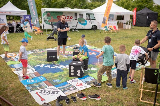 Dzieci grają na wielkiej planszy rozłożonej na trawie w grę Monopoly Mazowsze