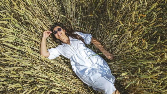 Renata Drogosz w okularach przeciwsłonecznych leży w pszenicy