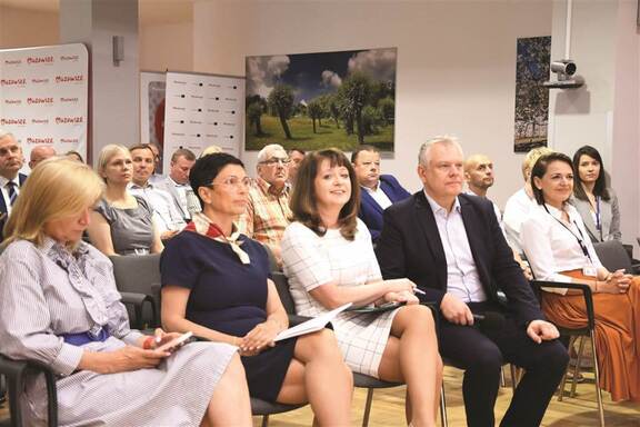 Członek zarządu województwa mazowieckiego Janina Ewa Orzełowska siedzi razem z innymi uczestnikami spotkania.