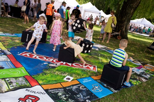 Grupka dzieci bawi się na wielkiej planszy gry monopoly