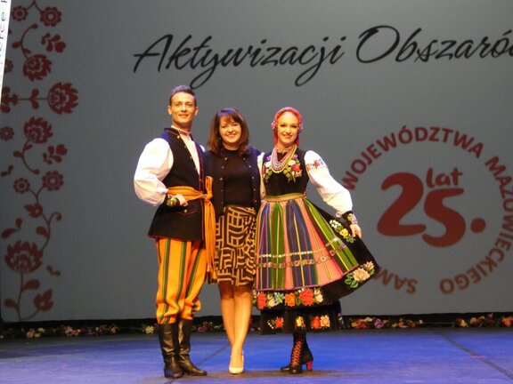 Członek zarządu Janina Ewa Orzełowska na scenie z parą tancerzy zespołu Mazowsze