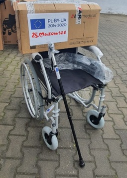 wózek inwalidzki, na którym jest paczka z oznaczeniem projektu PL-BY-UA oraz logiem Mazowsza