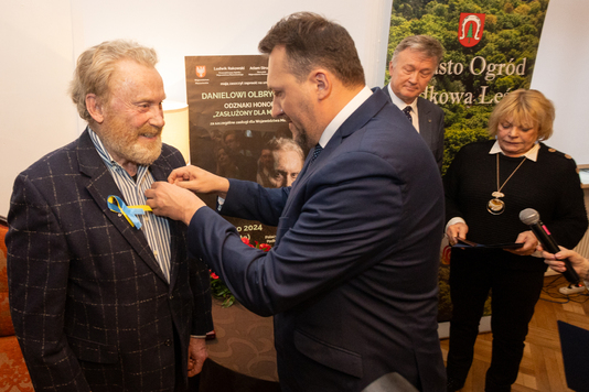 Wiceprzewodniczący Marcin Podsędek przypina odznakę do klapy garnituru Daniela Olbrychskiego.